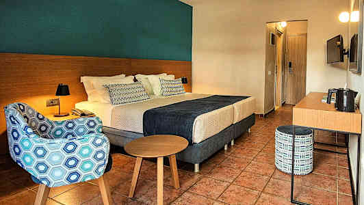 Et hotellrom med en dobbeltseng, lenestol, bord og skrivebord. (AI-generert tekst)