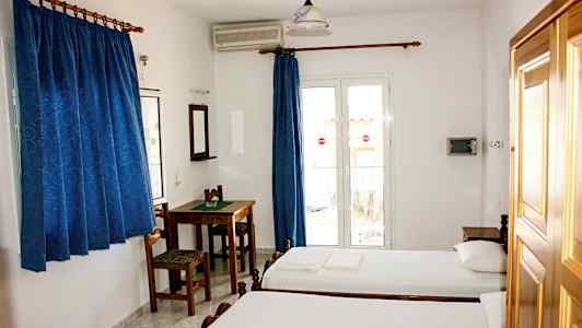 Et hotellrom med to enkeltsenger, et bord med stoler, blå gardiner og en balkongdør. (AI-generert tekst)