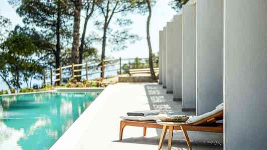 En solseng og et lite bord ved et basseng, omgitt av søyler og trær. (AI-generert tekst)