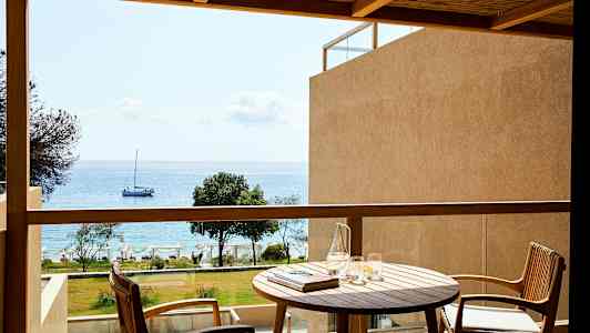 En balkong med utsikt mot havet, med et bord og to stoler. (AI-generert tekst)