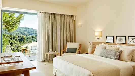 Et hotellrom med en dobbeltseng, sittemøbler og et stort vindu med utsikt over et frodig landskap. (AI-generert tekst)