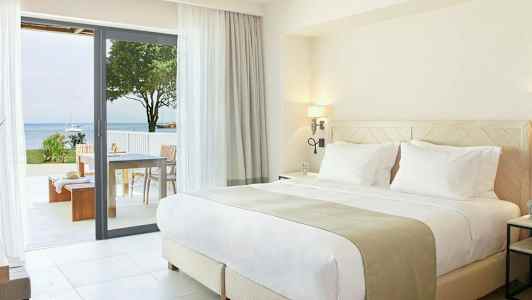 Moderne soverom med dobbeltseng og utgang til terrasse med havutsikt. (AI-generert tekst)