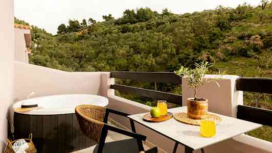 En balkong med et boblebad, et bord med saftglass og frukt samt utsikt over grønne områder. (AI-generert tekst)