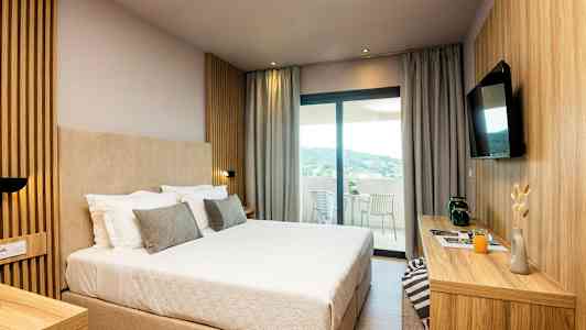 Hotellrom med en stor seng, moderne innredning og utsikt mot en terrasse. (AI-generert tekst)