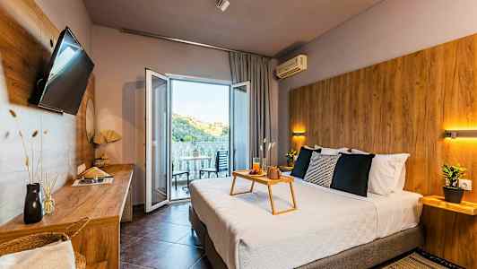 Moderne hotellrom med dobbeltseng, sittemøbler på balkongen og utsikt over en grønn ås. (AI-generert tekst)