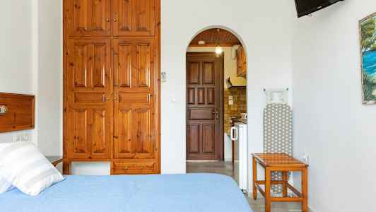 Et rom med en seng, treskap, strykebrett og en åpning til et kjøkken. (AI-generert tekst)