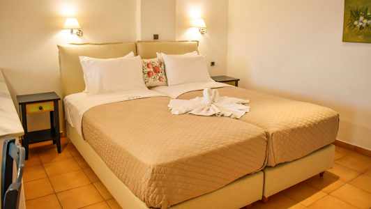 Et hotellrom med to enkeltsenger plassert sammen som en dobbeltseng, dekket med beige sengeteppe og dekorative puter. Håndklær formet som en svane ligger på sengen. (AI-generert tekst)