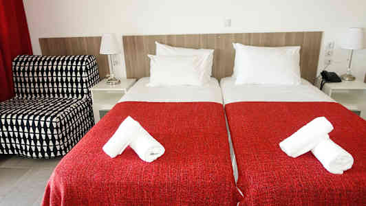 To enkeltsenger med røde sengetepper og hvite håndklær på toppen. (AI-generert tekst)