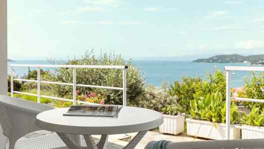 Utsikt over havet fra en terrasse med et bord og stoler. (AI-generert tekst)