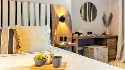 Et moderne hotellrom med tredekor, en seng med dekorative puter, et skrivebord med speil og dekorative gjenstander, og grønne druer på et fat. (AI-generert tekst)