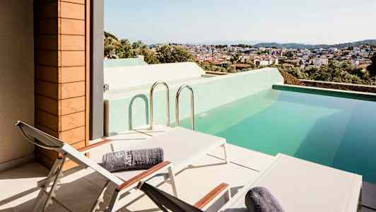 Terrasse med solsenger og et basseng, med utsikt over en by. (AI-generert tekst)