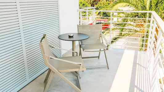 En balkong med to beige stoler og et svart rundt bord. (AI-generert tekst)