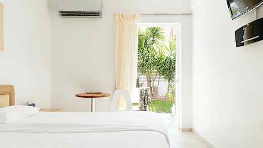 Et lyst hotellrom med en seng, et bord og en åpning mot en hage. (AI-generert tekst)