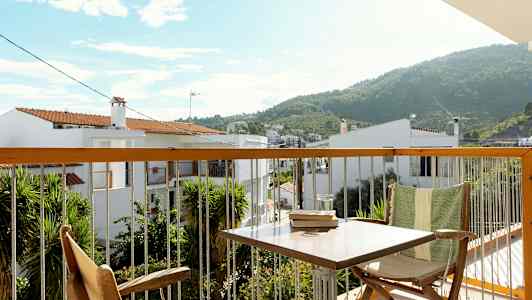 Utsikt fra en balkong med møbler og vegetasjon, samt hus og fjell i bakgrunnen. (AI-generert tekst)
