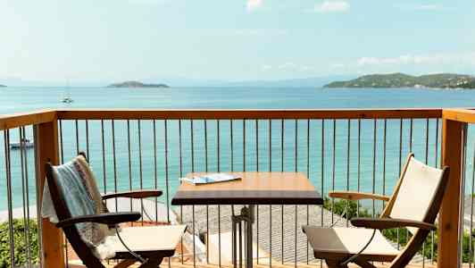 Utsikt fra en balkong med to stoler, et bord og havet i bakgrunnen. (AI-generert tekst)