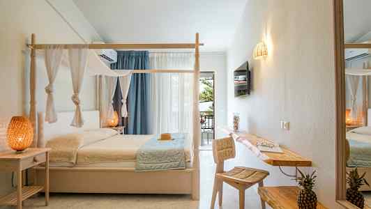 Et hotellrom med en himmelseng, dekorative lamper og en skrivebordflate med stol samt en bolle med to ananas. (AI-generert tekst)