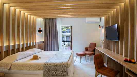 Et moderne hotellrom med en dobbeltseng, trepaneler på veggene og utsikt mot en balkong. Rommet har en TV og en komfortabel sitteplass. (AI-generert tekst)