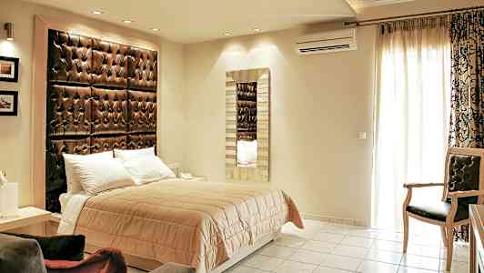 Et soverom med en dobbeltseng, en stor polstret sengegavl og et speil på veggen. (AI-generert tekst)