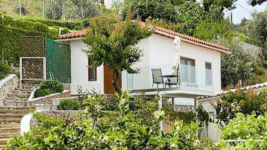 Hvitt hus med balkong, omgitt av hage og grøntområder. (AI-generert tekst)