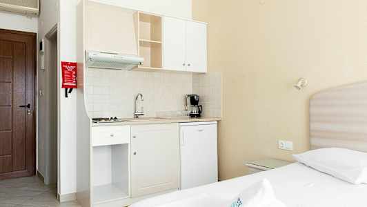 Lite kjøkkenkrok med hvite kjøkkenskap i et rom med en seng. (AI-generert tekst)