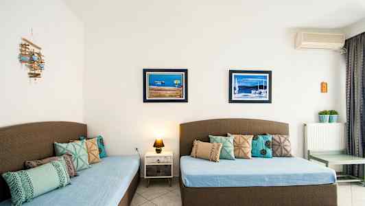 To senger med blå sengetepper og dekorative puter, to bilder med maritime motiv på veggen. (AI-generert tekst)