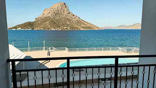 Bildet viser utsikten fra en balkong over et basseng og havet, med en fjellrik øy i bakgrunnen. (AI-generert tekst)