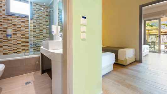 Utsikt mot et baderom med flislagte vegger og et tilstøtende soverom med senger. (AI-generert tekst)