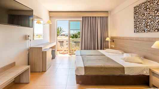 Hotellrom med to senger, skrivebord, TV og en åpning til en balkong. (AI-generert tekst)