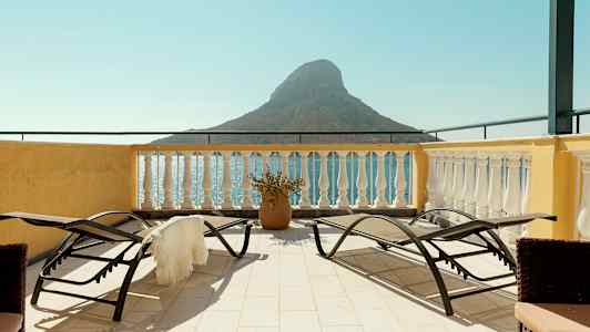 Terrasse med solsenger og utsikt over havet og en liten fjellformasjon. (AI-generert tekst)