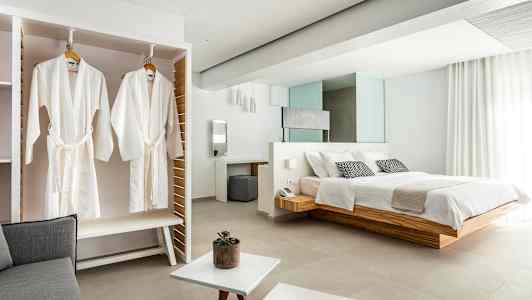 Bilde av et elegant hotellrom med en stor seng, hvite badekåper som henger i et skap og lyse moderne møbler. (AI-generert tekst)