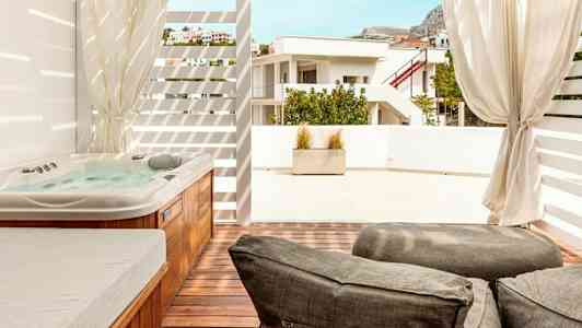 Bildet viser en terrasse med et boblebad, solsenger og utsikt mot nabobygningen. (AI-generert tekst)