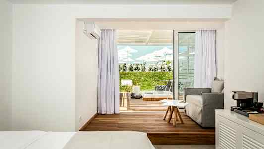 Et hotellrom med et moderne soverom og sittegruppe samt en terrasse utenfor med plen og solsenger. (AI-generert tekst)