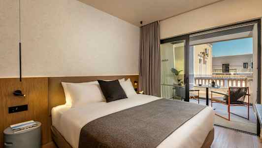 Et hotellrom med en dobbeltseng og en balkong med sitteplasser. (AI-generert tekst)