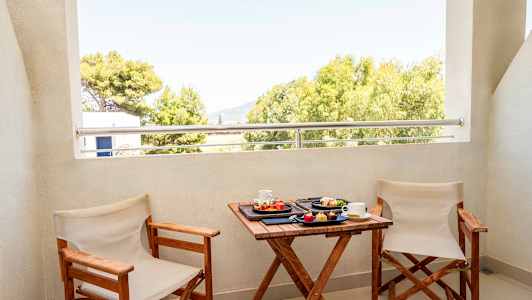 To stoler og et bord med frokost serveres på en balkong med utsikt over trær. (AI-generert tekst)