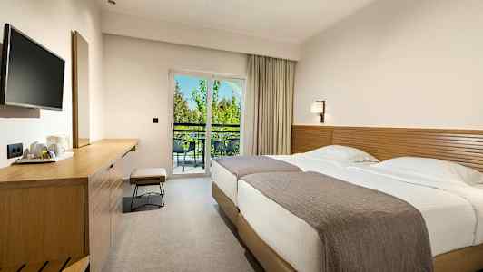 Et hotellrom med to senger, en arbeidsbenk og en balkong med utsikt. (AI-generert tekst)