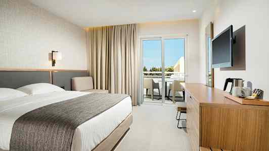 Moderne hotellrom med dobbeltseng, sitteområde og møblert balkong. (AI-generert tekst)