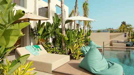 Et basseng omgitt av grønne planter og solmøbler. (AI-generert tekst)