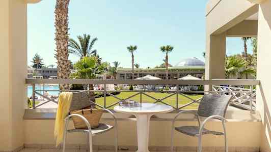 Utsikt fra balkongen mot en hage med palmer og et basseng. (AI-generert tekst)