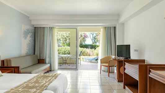 Et hotellrom med en dobbeltseng, sofamøbler, TV og en terrasse med utsikt mot hagen. (AI-generert tekst)