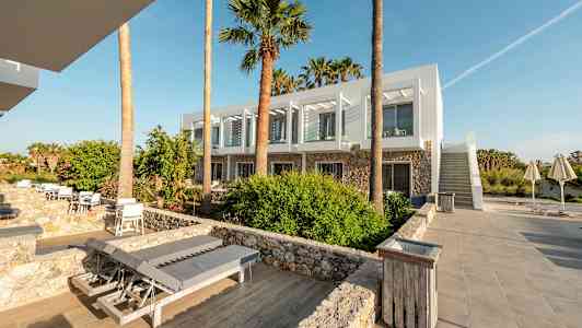 Et moderne hotell med hvite fasader og store vinduer omgitt av palmer og steinlagte stier. (AI-generert tekst)