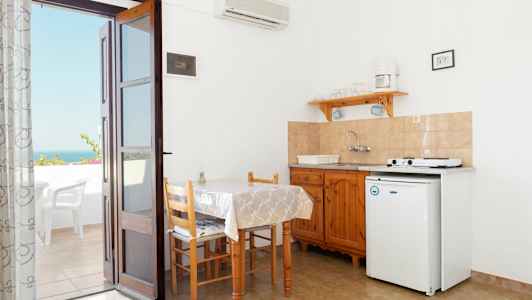 Et liten kjøkkenområde med bord, stoler og en kokekrok. En dør fører ut til en terrasse med utsikt. (AI-generert tekst)