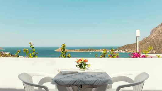 Utsikt over havet fra en balkong med et bord, to stoler og en vase med blomster. (AI-generert tekst)