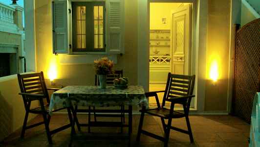 En terrasse med et bord og to stoler, opplyst om kvelden, med en åpning mot et interiør. (AI-generert tekst)