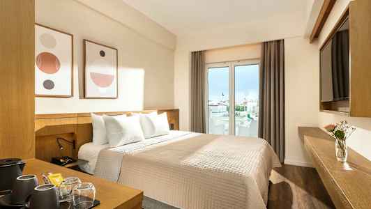 Et hotellrom med en dobbeltseng, moderne innredning og vinduer med utsikt mot byen. (AI-generert tekst)