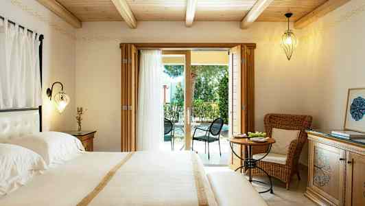 Et soverom med dobbeltseng, lyse møbler og glassdører som fører til en møblert uteplass. (AI-generert tekst)