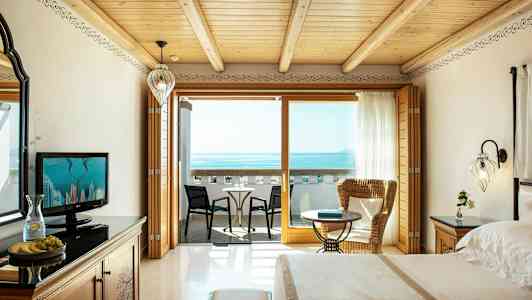 Et hotellrom med utsikt over havet, inkludert en balkong med sitteplasser. (AI-generert tekst)