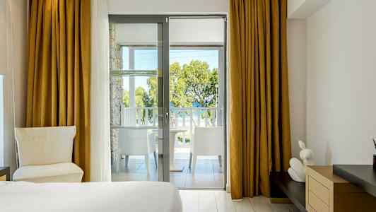 Hotellrom med utsikt fra balkong mot trær og hav. (AI-generert tekst)