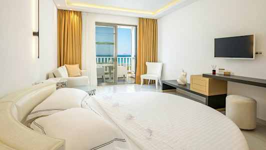 Interiør av et hotellrom med en seng, sittemøbler og en balkong med havutsikt. (AI-generert tekst)