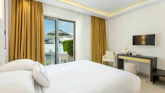 Hotellrom med hvit innredning, en dobbeltseng, skrivebord og utgang til terrasse. (AI-generert tekst)