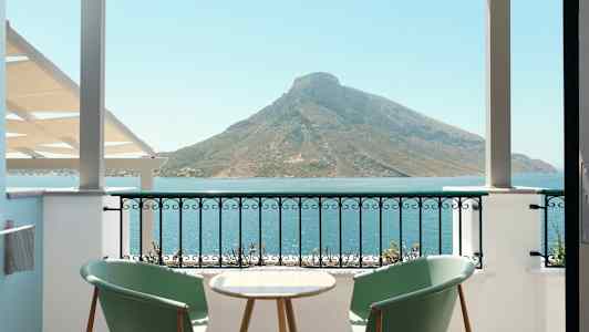 To stoler og et bord på en balkong med utsikt over havet og et fjell. (AI-generert tekst)